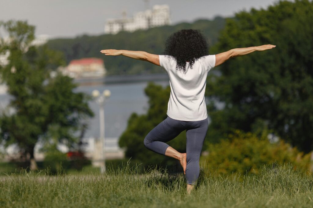 Woman performing yoga in a scenic park setting with lake and trees.