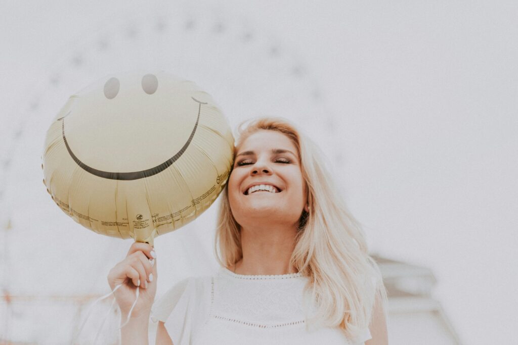 pexels-photo-1236678-1236678 Cheerful woman holding a smiley balloon outdoors on a sunny day, exuding happiness and positivity.