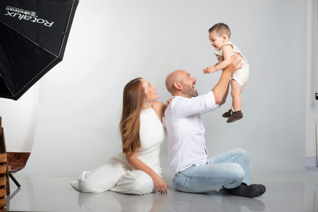 A joyful family portrait with parents and baby in a professional studio setting.