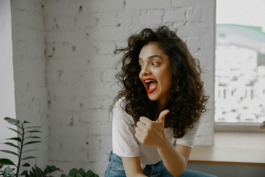 Cheerful woman with curly hair expressing positivity with a thumbs-up gesture.