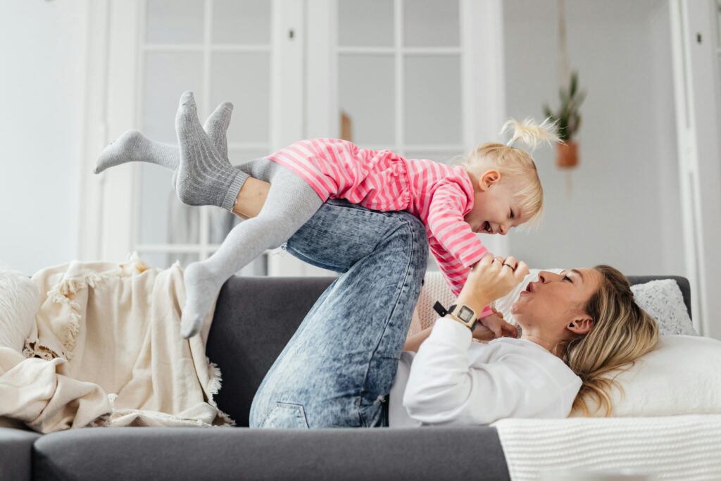 A joyful mother and daughter spend playful moments together on a couch, enhancing their bond.