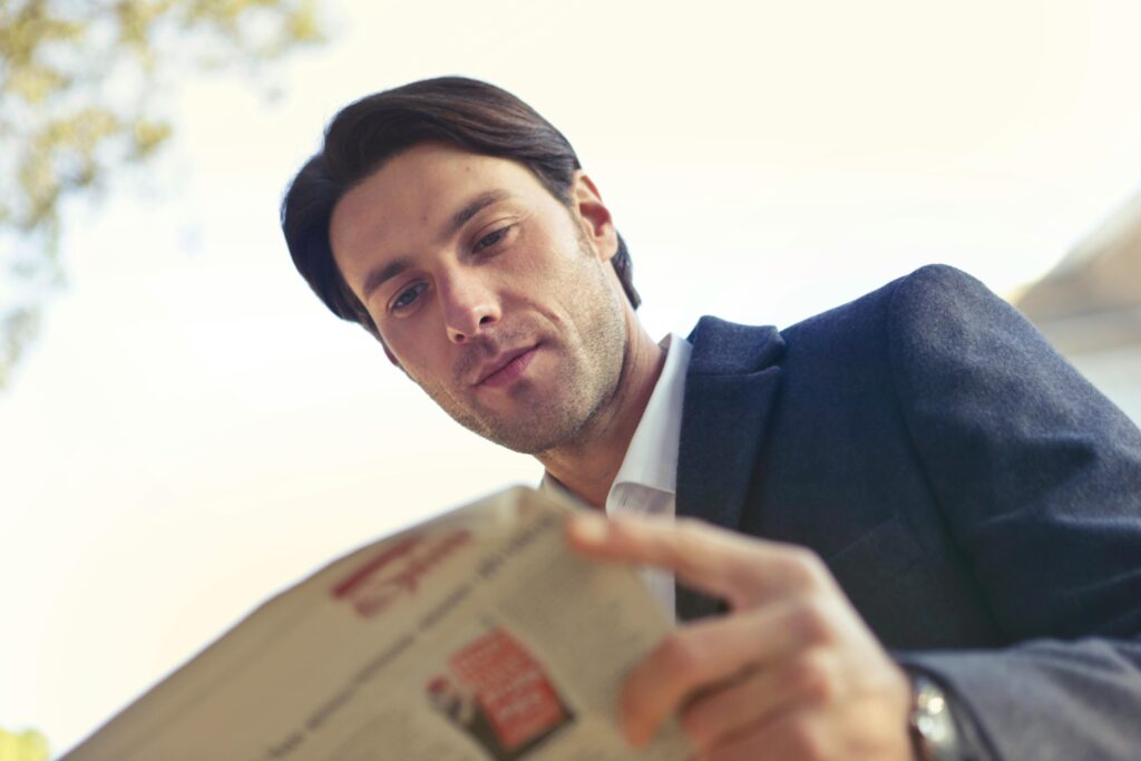 Adult man in formal attire reading a newspaper outdoors in Rome, Italy, during the day.