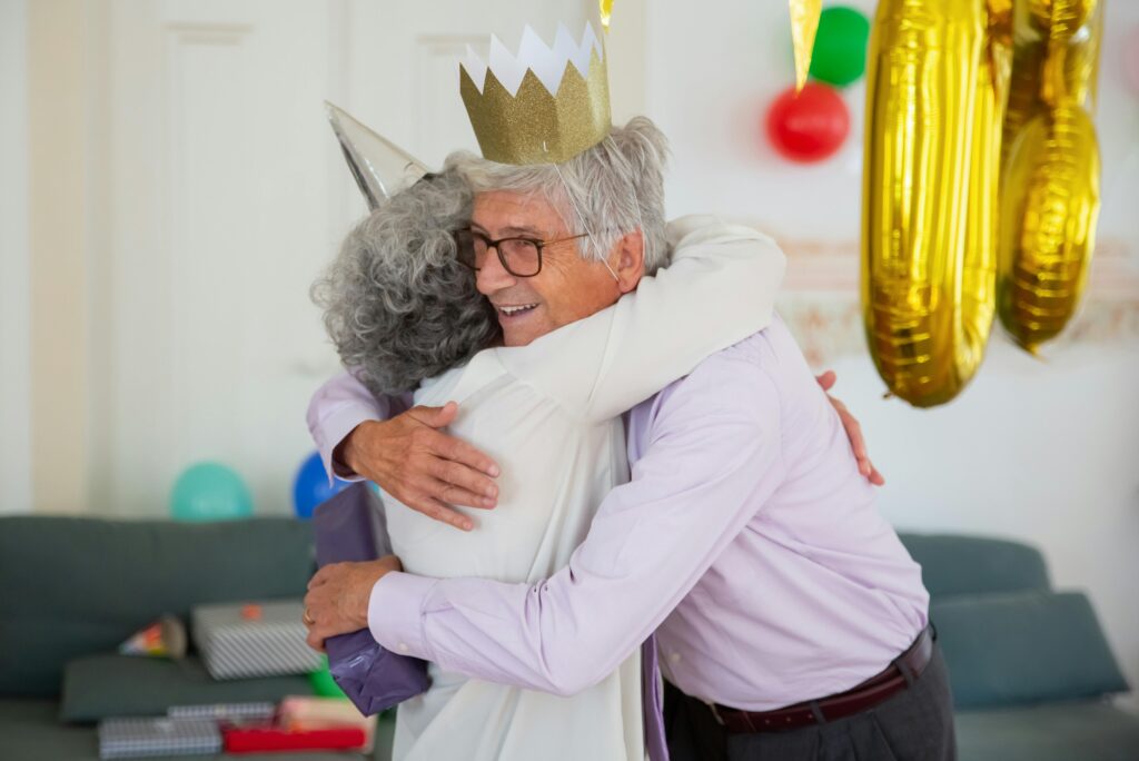 Heartwarming scene of a senior couple hugging at an indoor birthday party with colorful decorations.